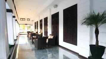 A corridor with a polished floor, dark wooden shutters, and a potted palm tree.