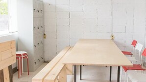 A room with a long wooden table, benches, and red chairs. There are electrical panels on the wall and a window on the left. - Nikkosan BackPackers Inn - Hostel (Nikko)
