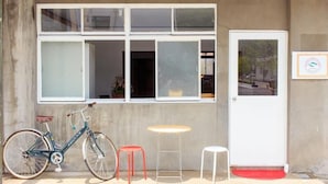 A bicycle parked outside a building with large windows, a door, and a small table with stools. - Nikkosan BackPackers Inn - Hostel (Nikko)