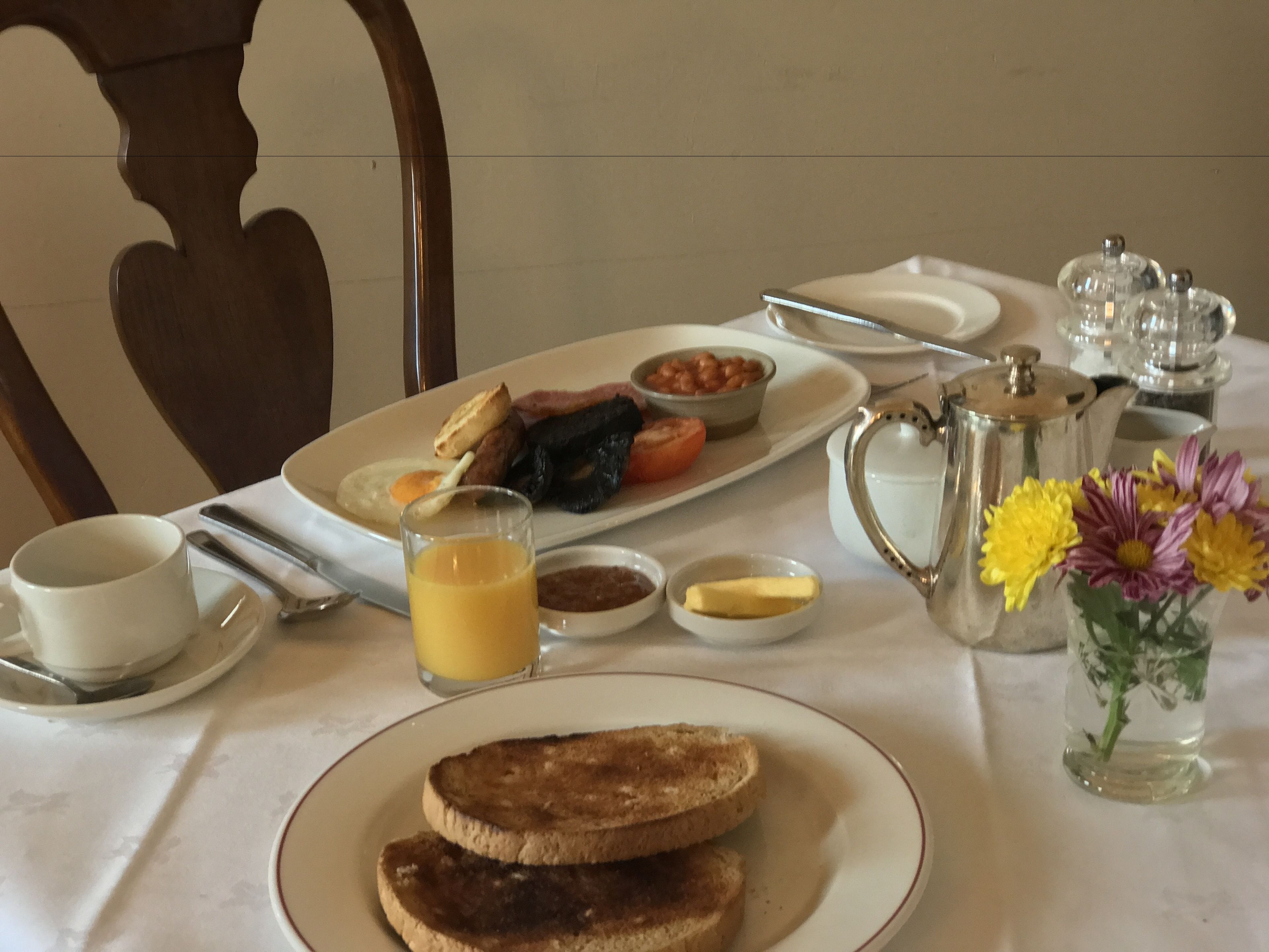A breakfast table with toast, eggs, beans, tomatoes, and a pitcher of juice.