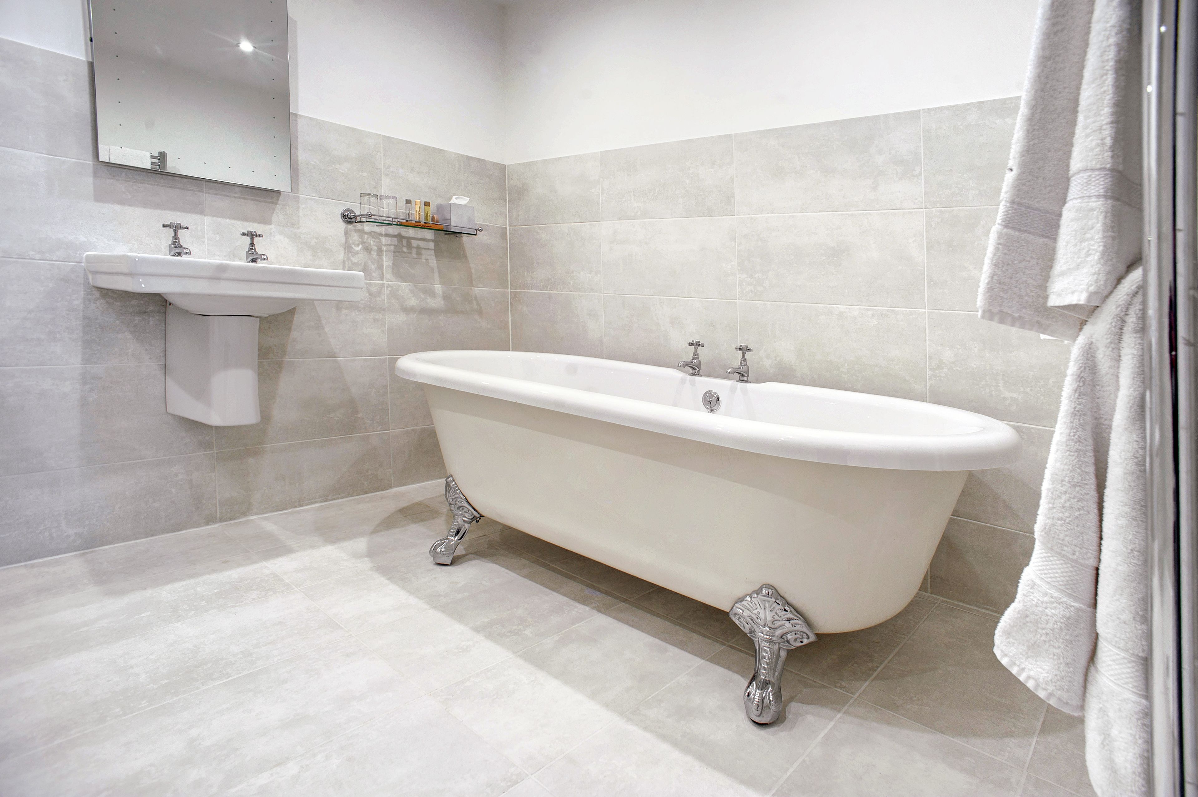 A bathroom with a freestanding bathtub, a pedestal sink, and a mirror above the sink.