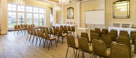 Un salón de conferencias con filas de sillas, una pizarra y candelabros.