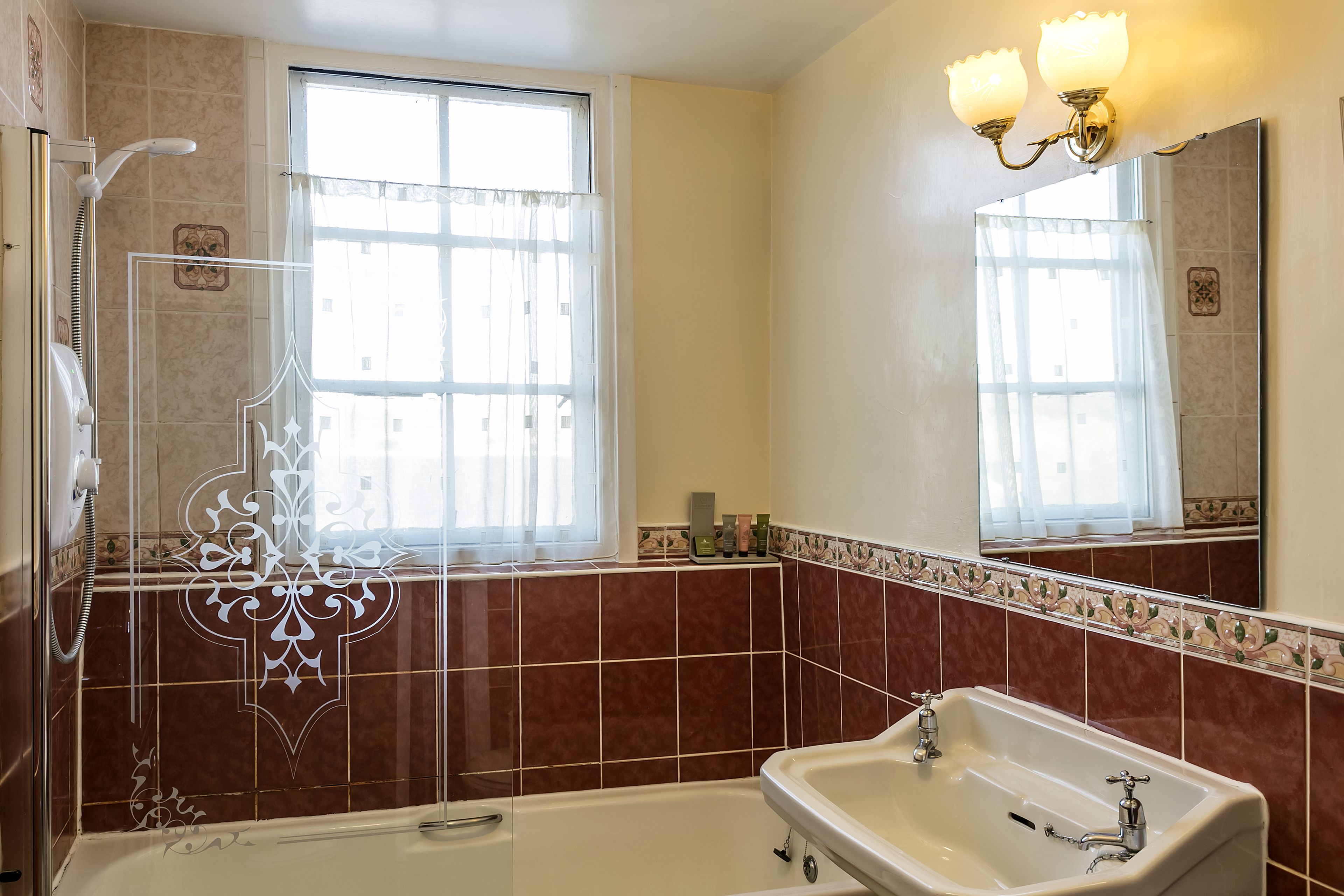 A bathroom with a bathtub, a sink, a shower, and a window with curtains.