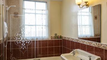 A bathroom with a bathtub, a sink, a shower, and a window with curtains.