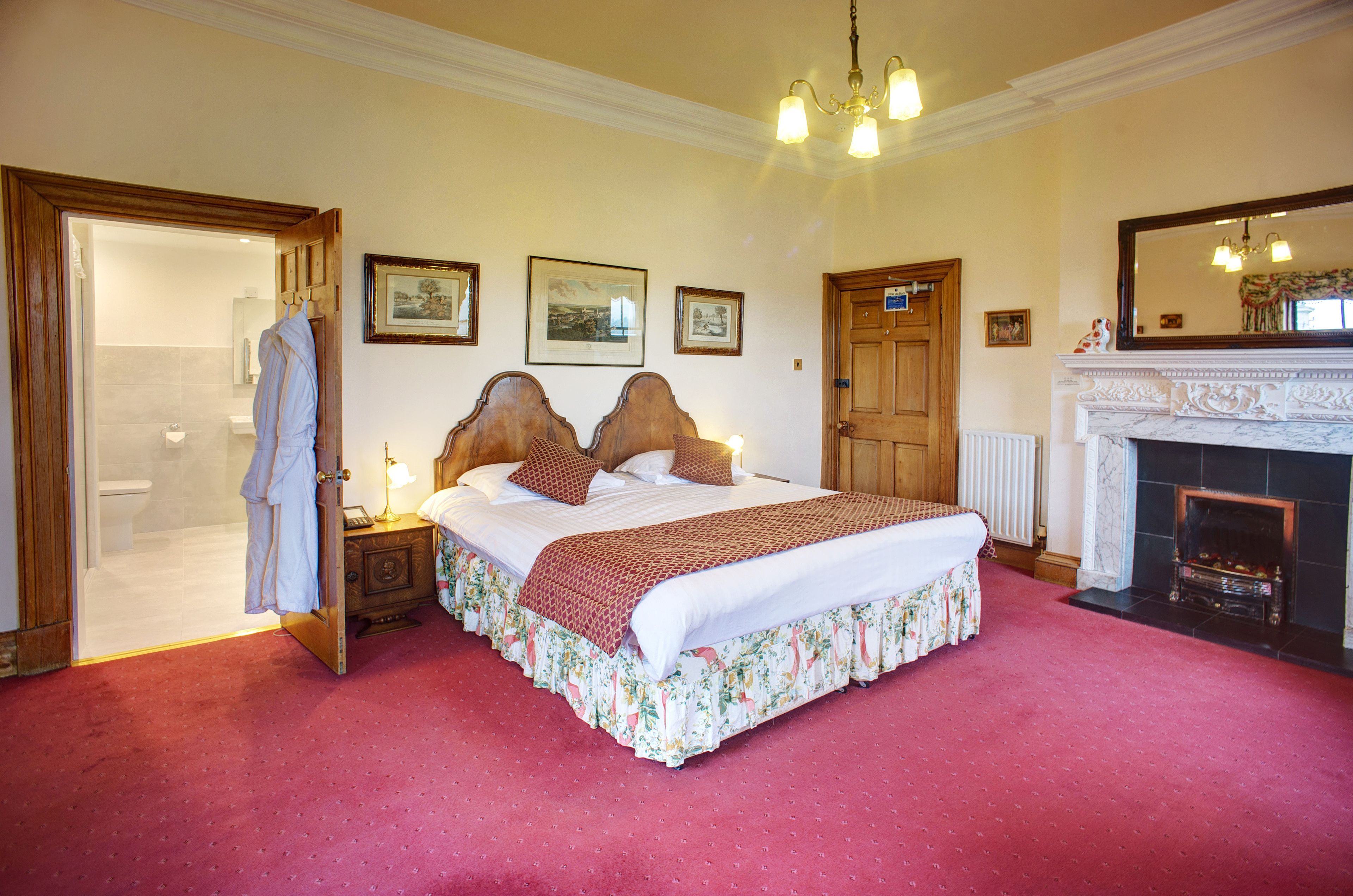 A bedroom with a large bed, a wooden door, a fireplace, and framed pictures on the wall.