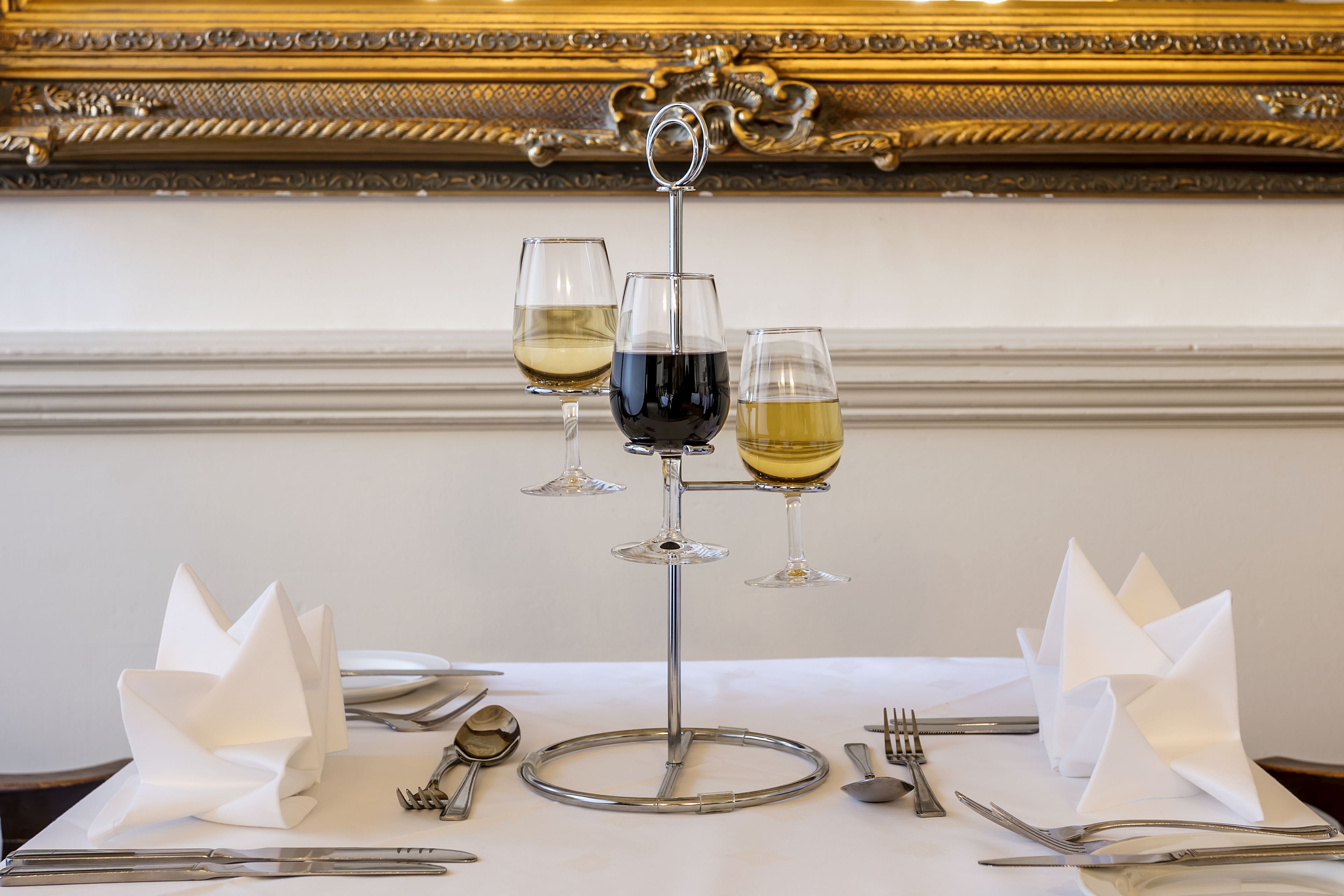 A dining table set with three wine glasses, a silver charger, and folded napkins.