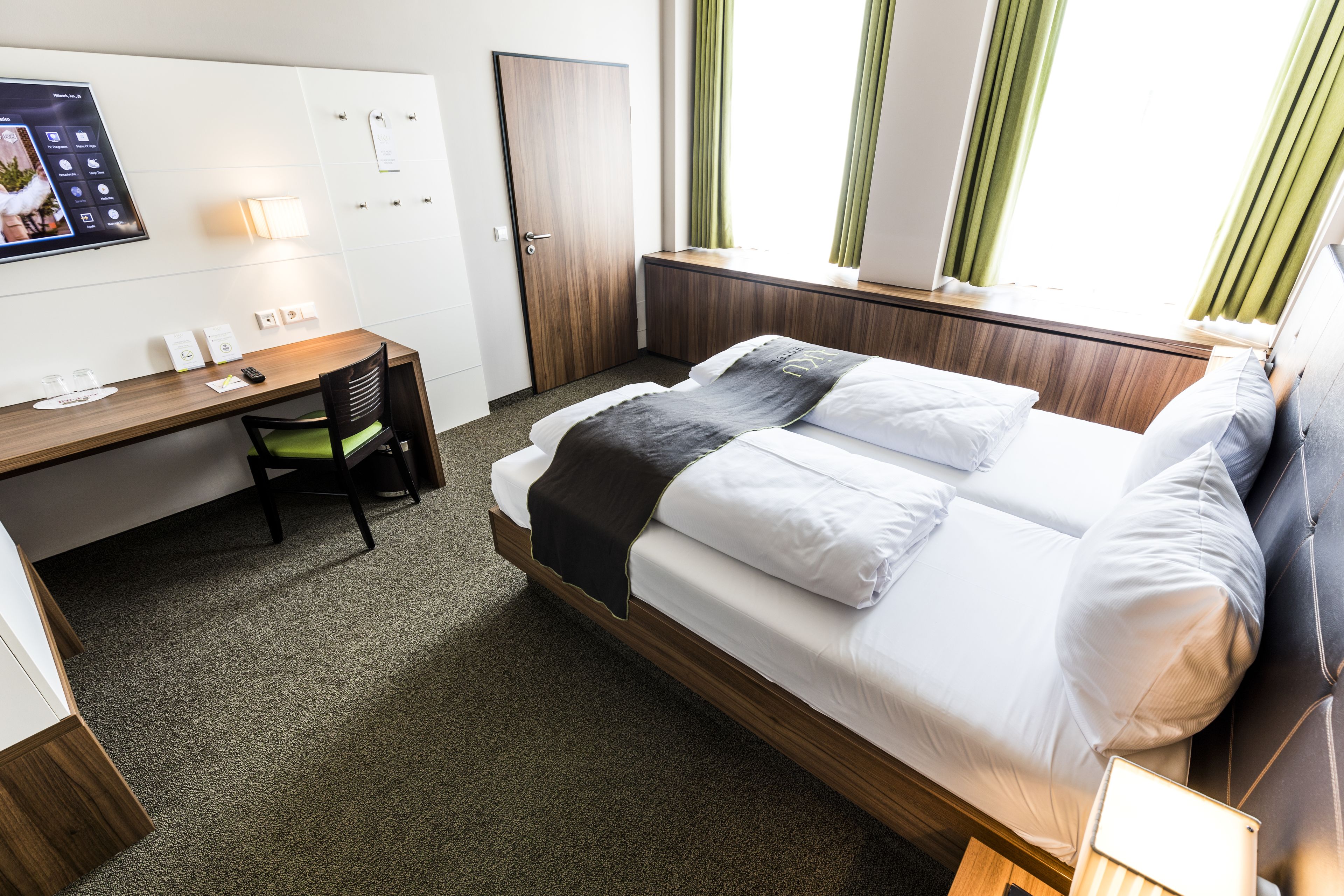 Une chambre d’hôtel avec un lit, un bureau, une chaise et une fenêtre avec des rideaux.