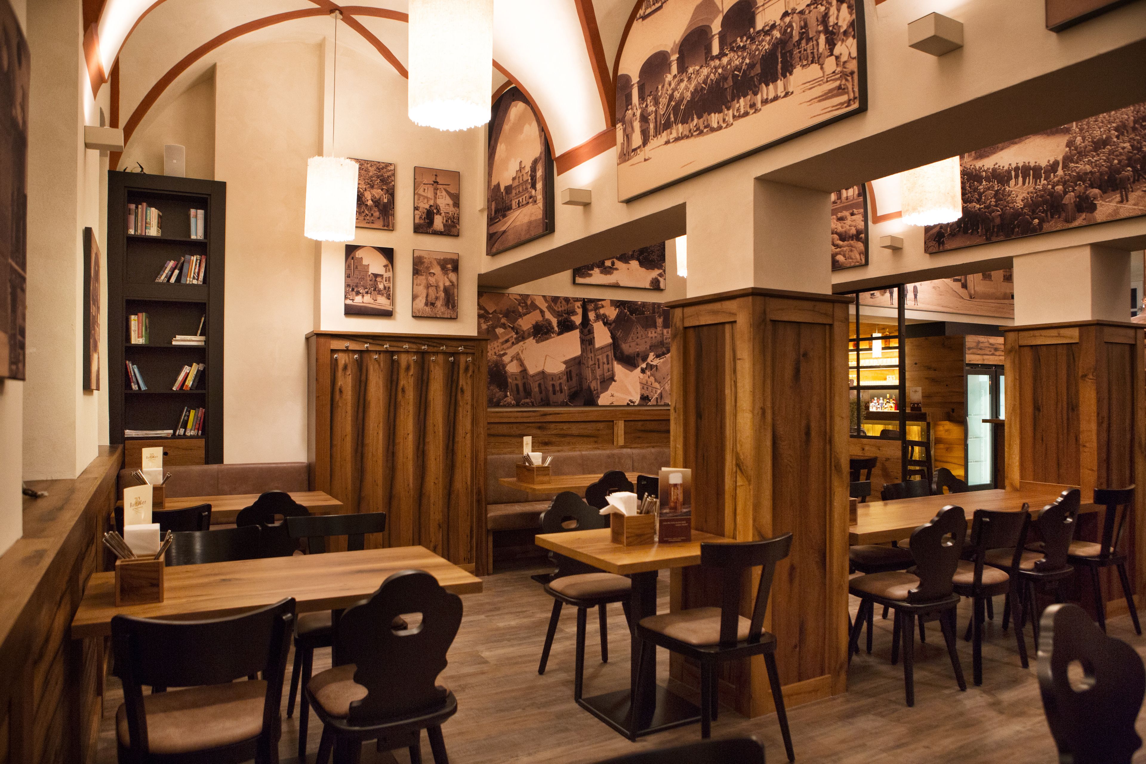 A restaurant with wooden tables and chairs, a bookshelf, and framed pictures on the walls.