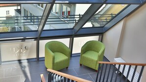 A modern interior with a glass ceiling, two green chairs, and a staircase with a wooden handrail. - RiKu HOTEL Weissenhorn (Weissenhorn)