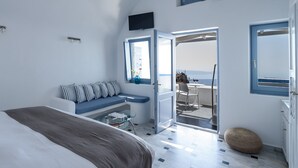 A bedroom with a bed, a seating area with a view, and a balcony with a table and chairs. - Pegasus Suites & Spa (Santorini)