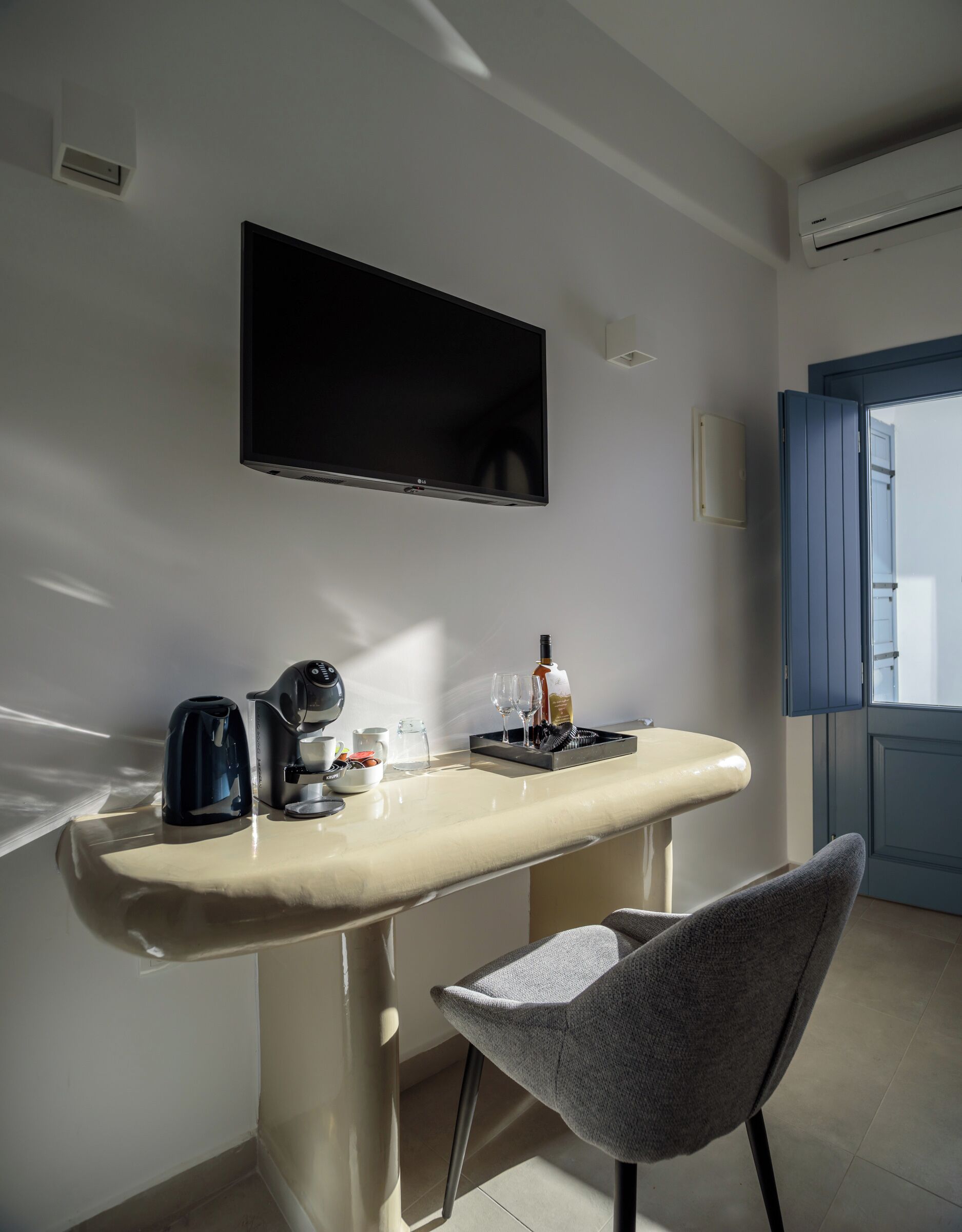 A modern kitchen with a flat-screen TV, a coffee machine, a wine bottle, and a glass set on the counter.