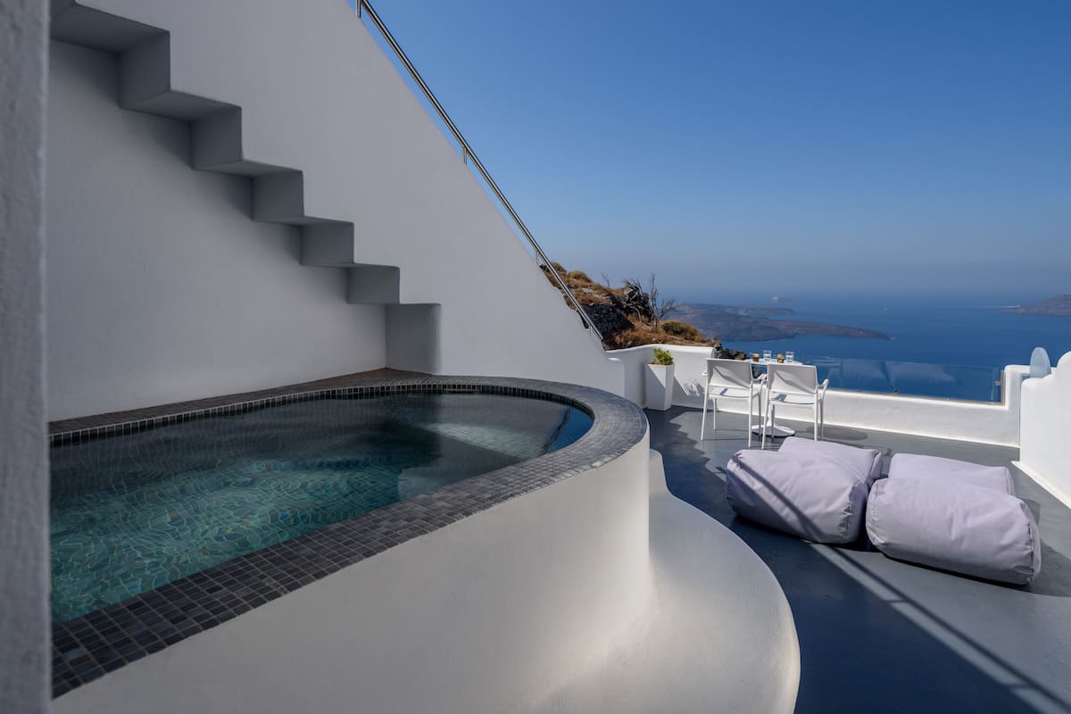 A modern infinity pool with a clear view of the sea, white steps leading up to the pool, and a seating area with cushions.