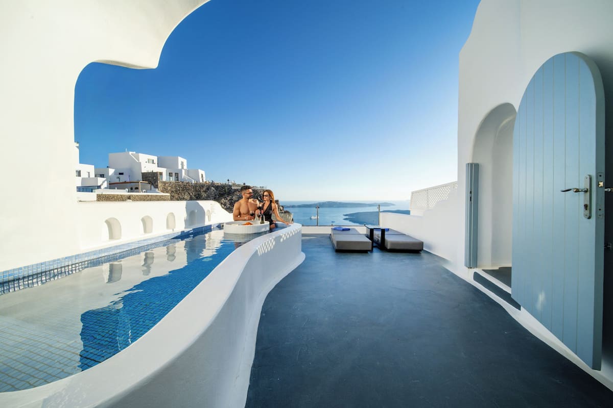 A modern infinity pool with a clear view of the sea, white architecture, and a blue door.