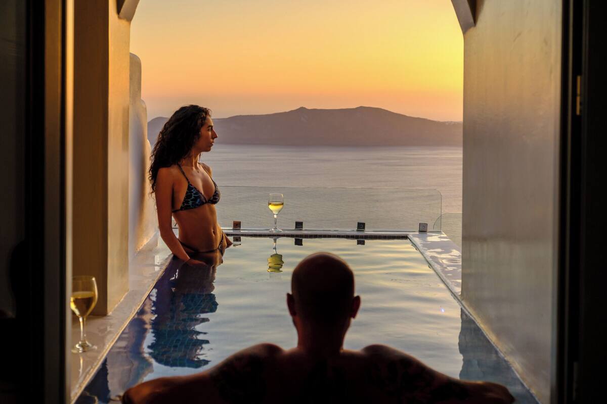 A man relaxing in a bathtub with a view of the sea and a sunset.