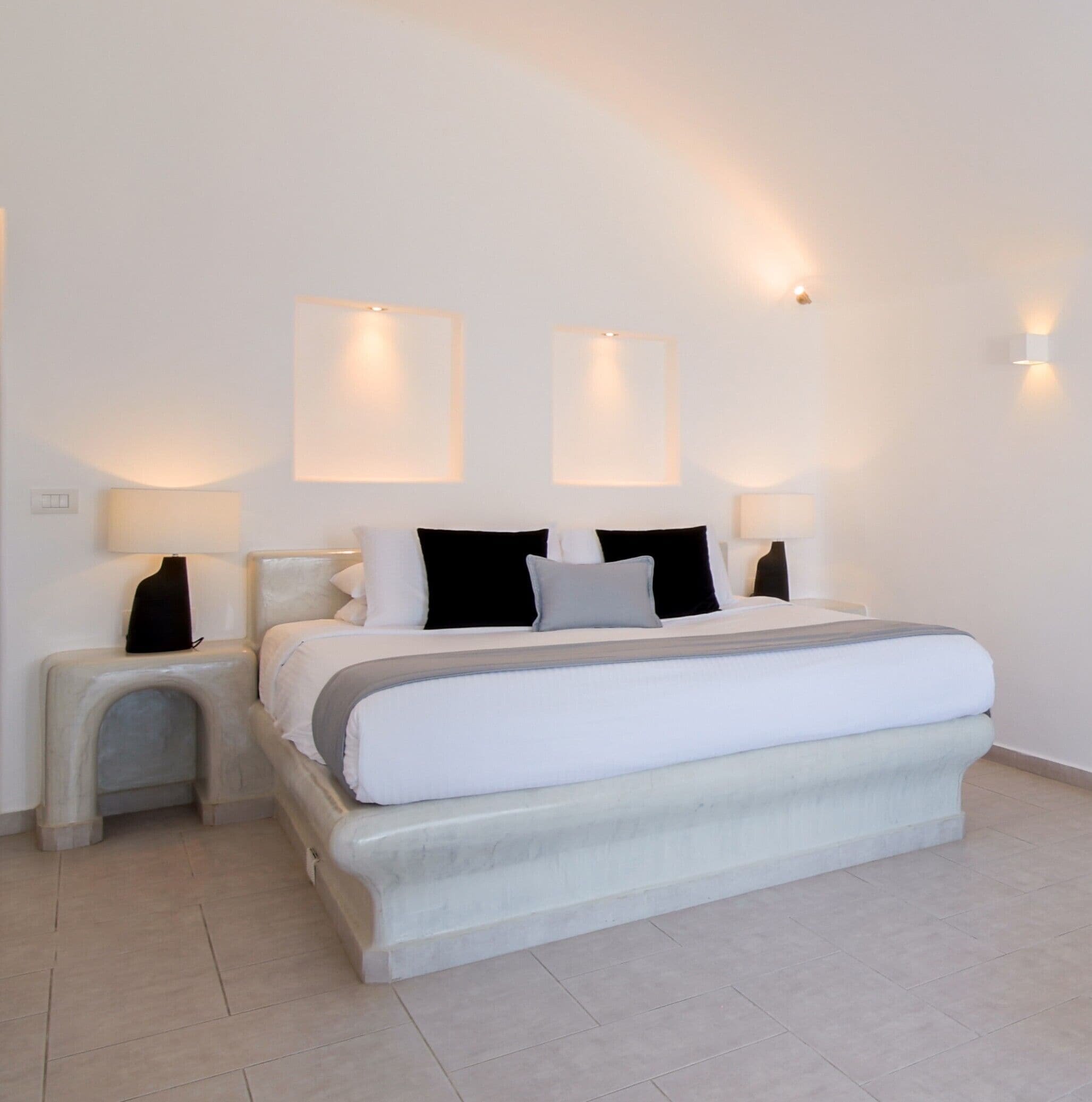 Un dormitorio moderno con una cama grande, dos mesitas de noche e iluminación empotrada en la pared.