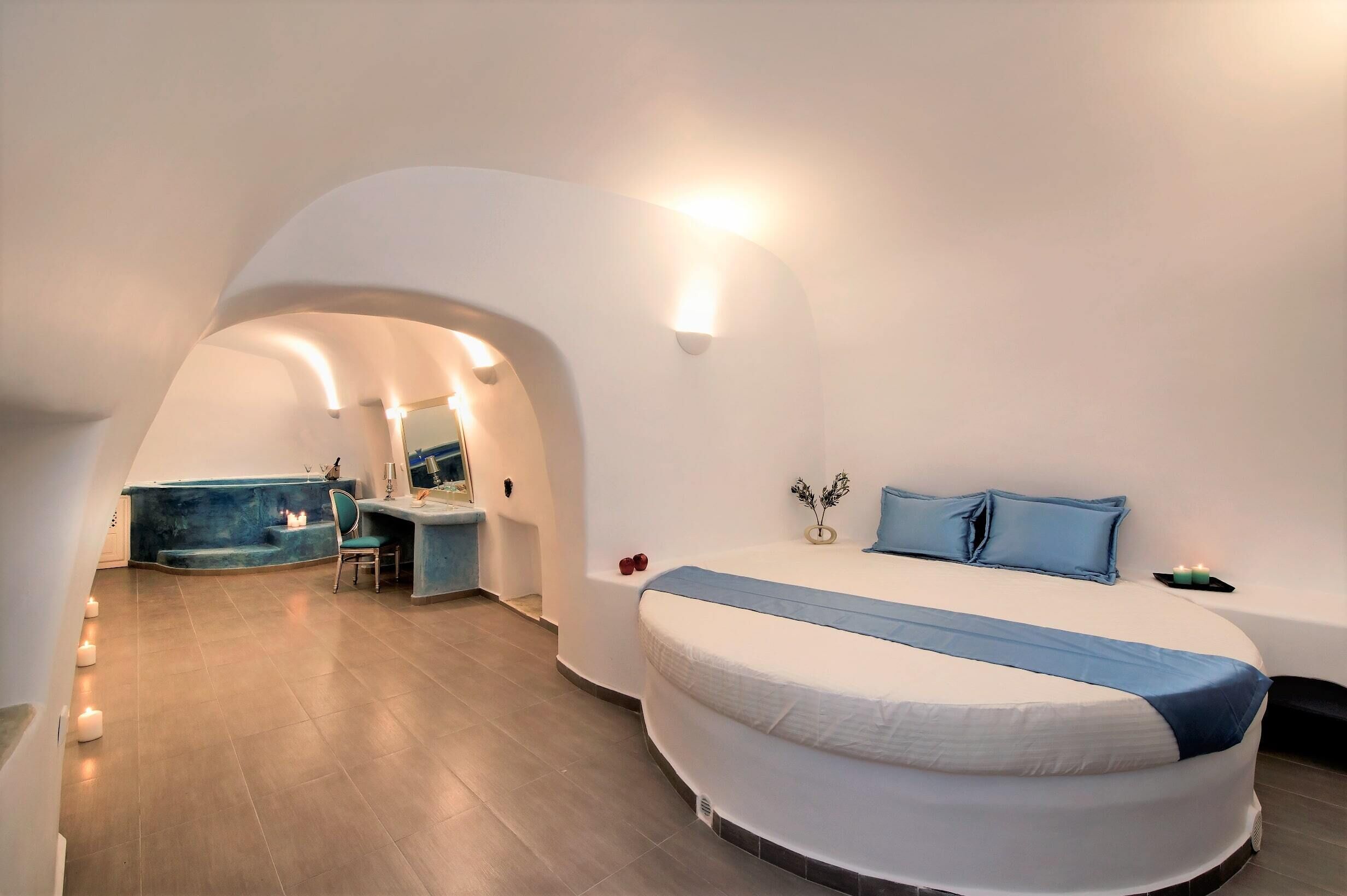 A modern bedroom with a curved bed, a small desk, and a bathroom visible through an archway.