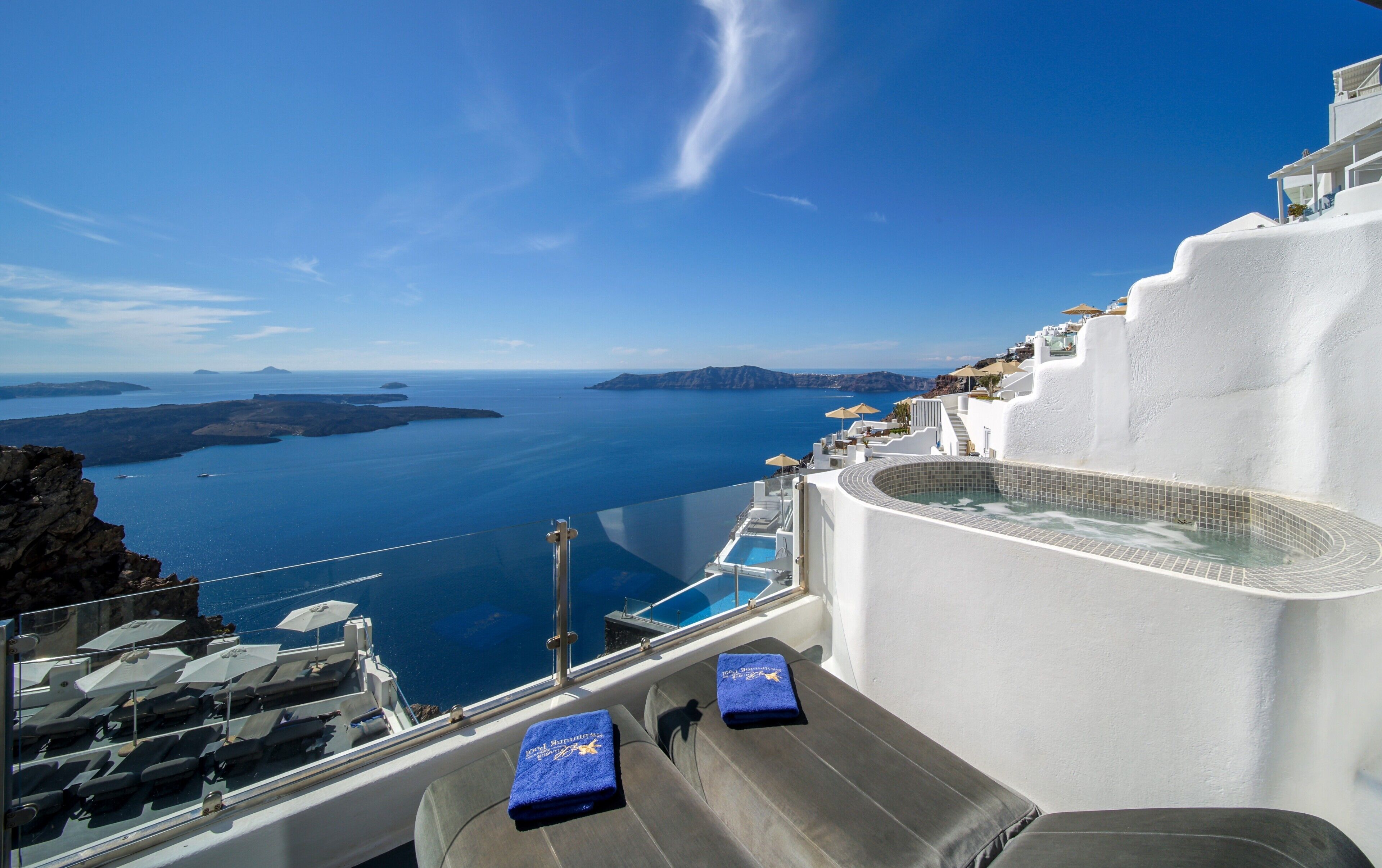 A view from a rooftop terrace with a pool, overlooking a coastal landscape with white buildings and the sea.