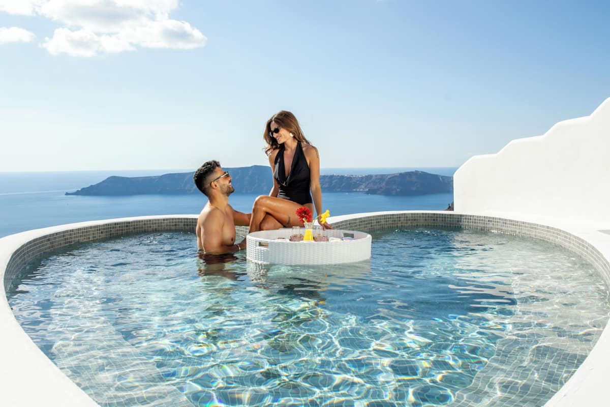 A heart-shaped infinity pool with clear blue water and a white edge, overlooking a scenic view of the sea and distant land.