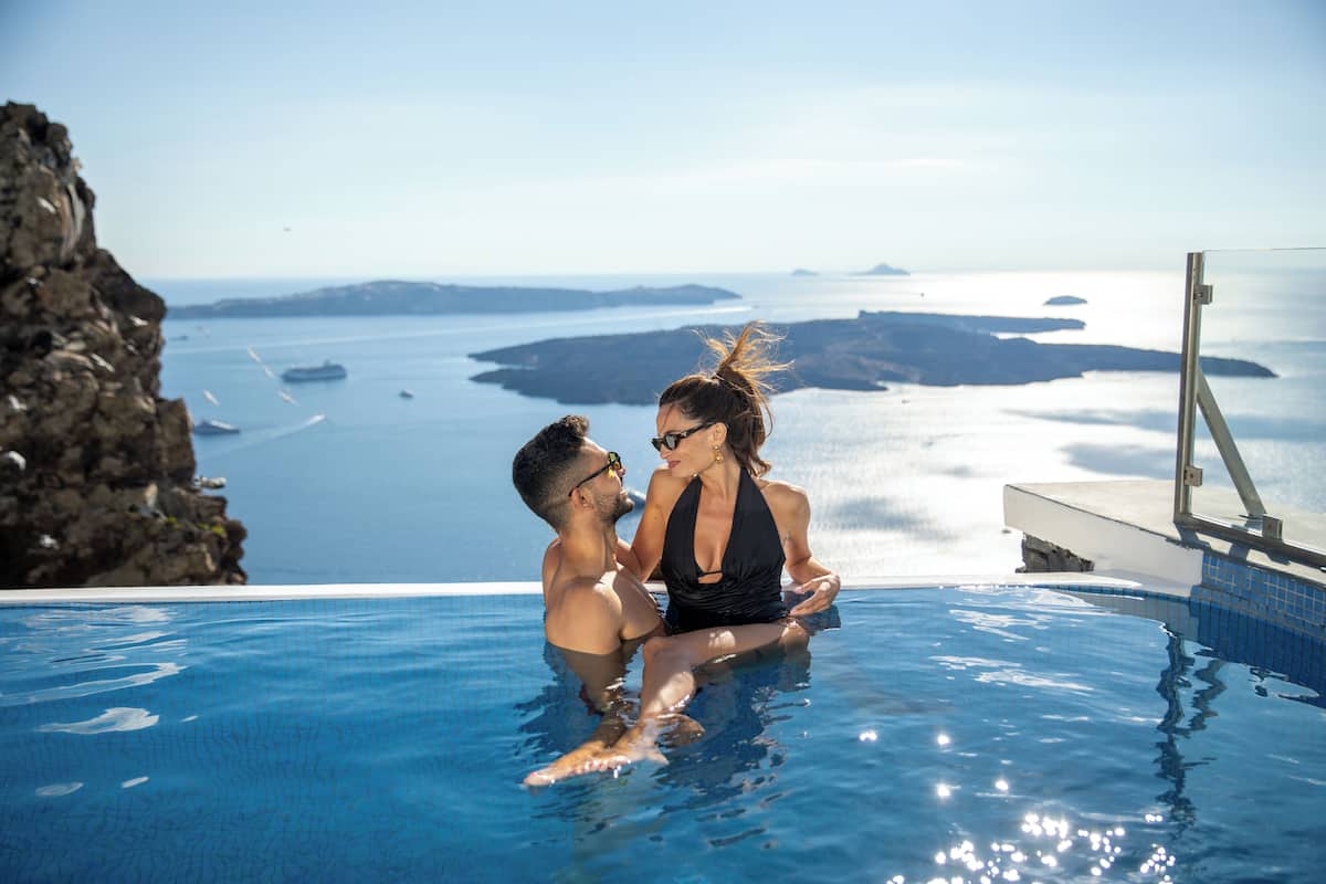 A couple in a swimming pool with a view of the sea and distant islands.