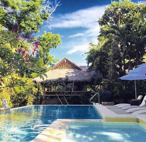 A swimming pool with a thatched-roof structure in the background, surrounded by lush greenery. - The Sun Villa Resort and Spa Hilltop (Boracay Island)