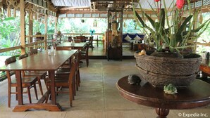 A wooden dining area with tables and chairs, a large woven planter with red flowers, and a view of the outdoors. - The Sun Villa Resort and Spa Hilltop (Boracay Island)