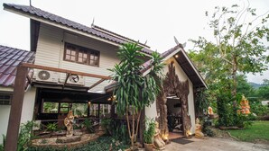 Una casa tradicional con techo de tejas, un porche cubierto y un jardín con estatuas y plantas.
