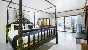 Una cama con dosel adornada con detalles tallados, un amplio ventanal con vistas al exterior y un televisor moderno sobre un soporte de madera.