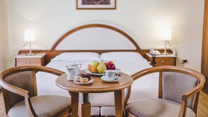 A hotel room with a bed, bedside tables, a table with breakfast, and two chairs.