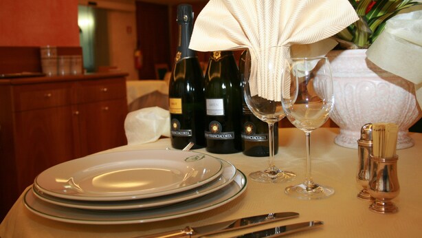 A table set with plates, wine glasses, and bottles, with a folded napkin and salt and pepper shakers.