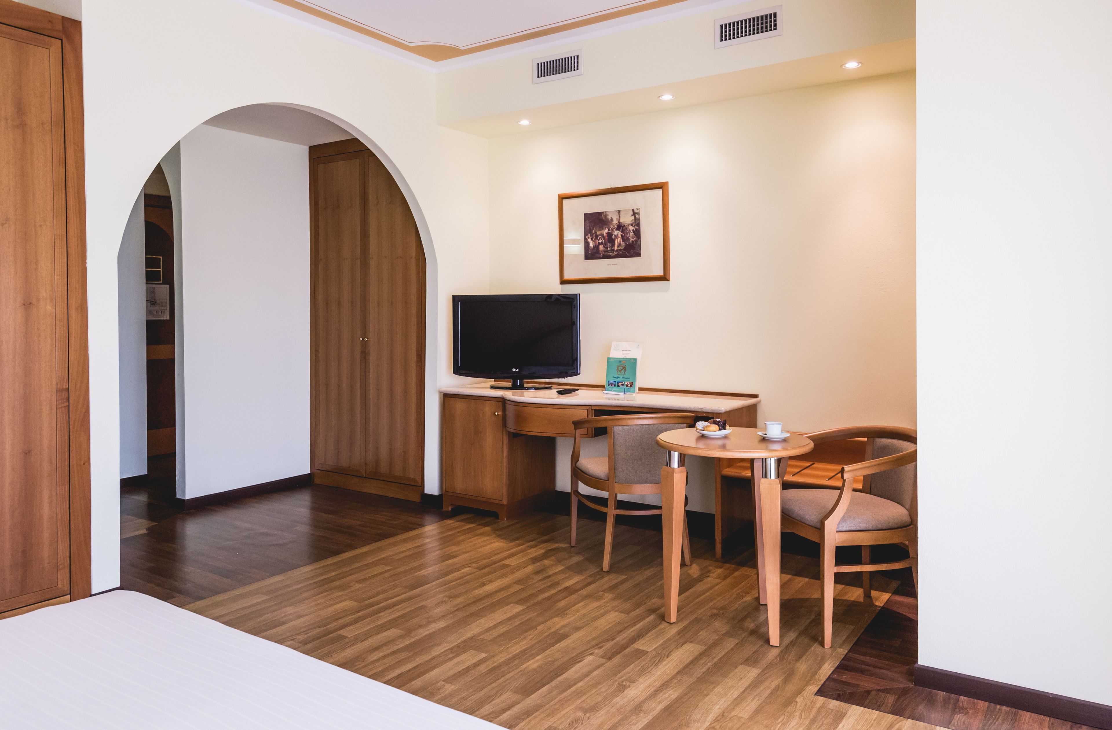 A hotel room with a wooden desk, two chairs, a television, and a framed picture on the wall.