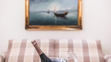 A bottle of champagne on a table with a striped cushion in the foreground and a framed painting of a boat on the wall in the background.
