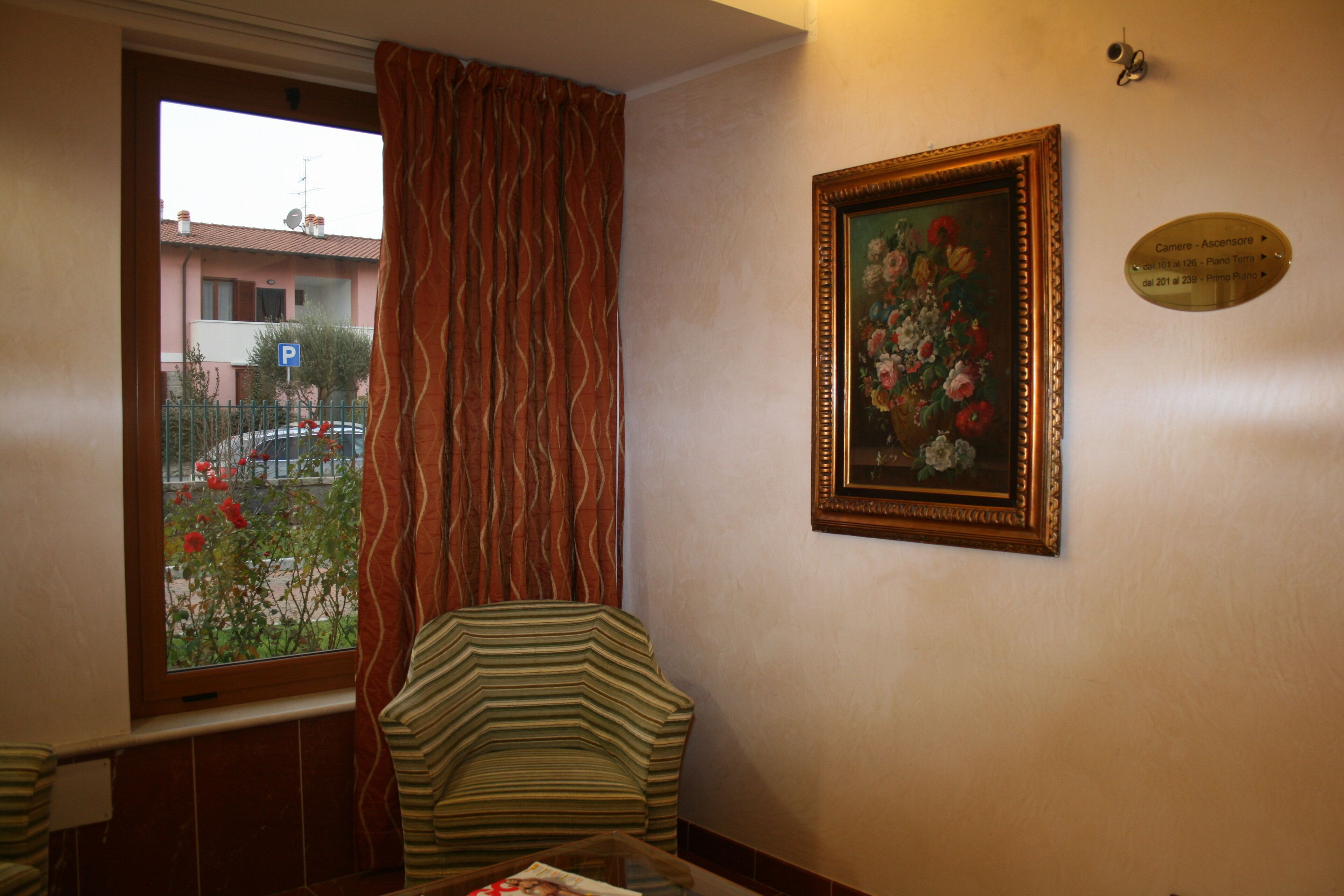 A room with a window, a chair, a framed painting, and a sign on the wall.