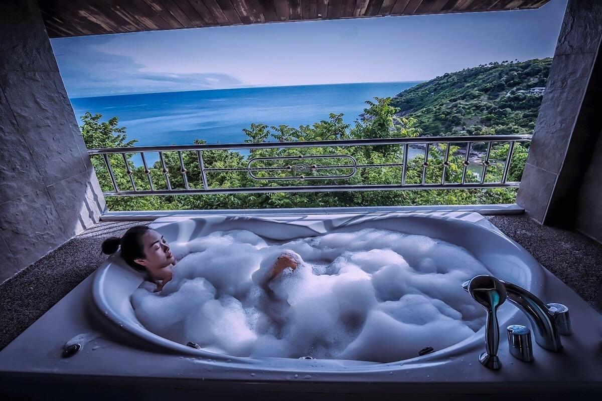 Una persona relajándose en un jacuzzi con una vista panorámica del océano y las colinas.