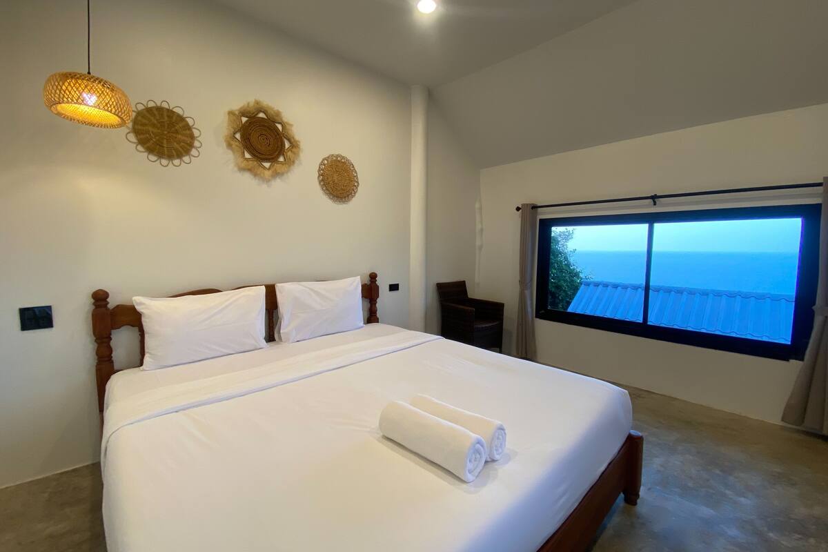 Un dormitorio con una cama grande, una ventana con vista al mar y adornos decorativos en la pared.