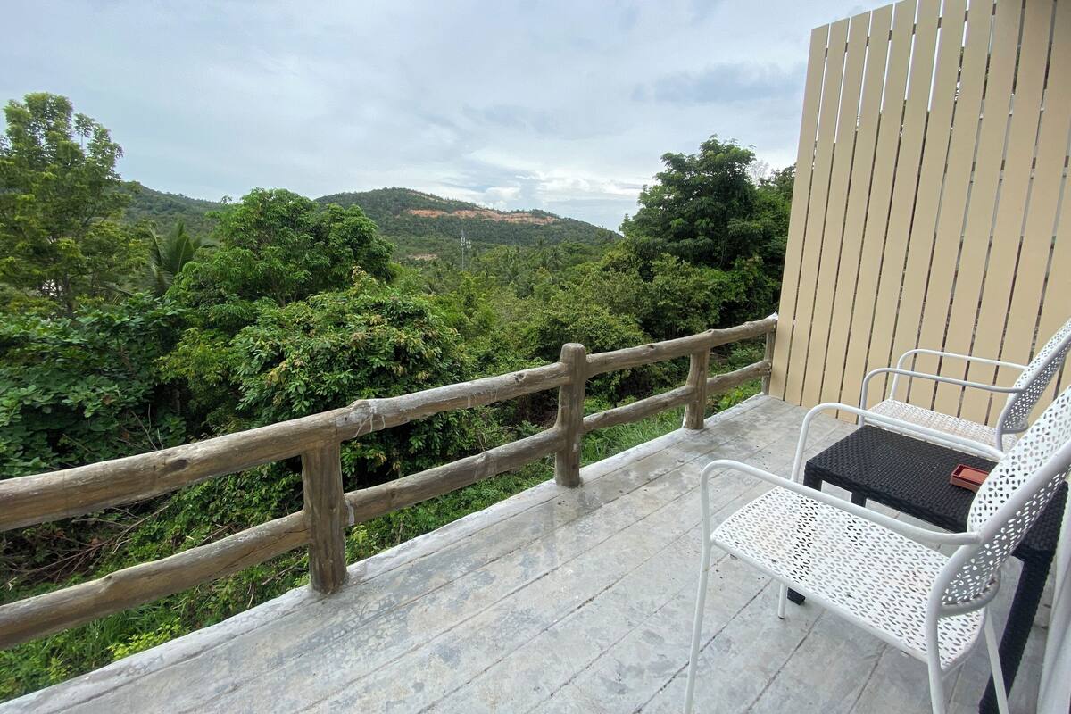 Un balcón con baranda de madera, una silla de metal blanco y una mesa.