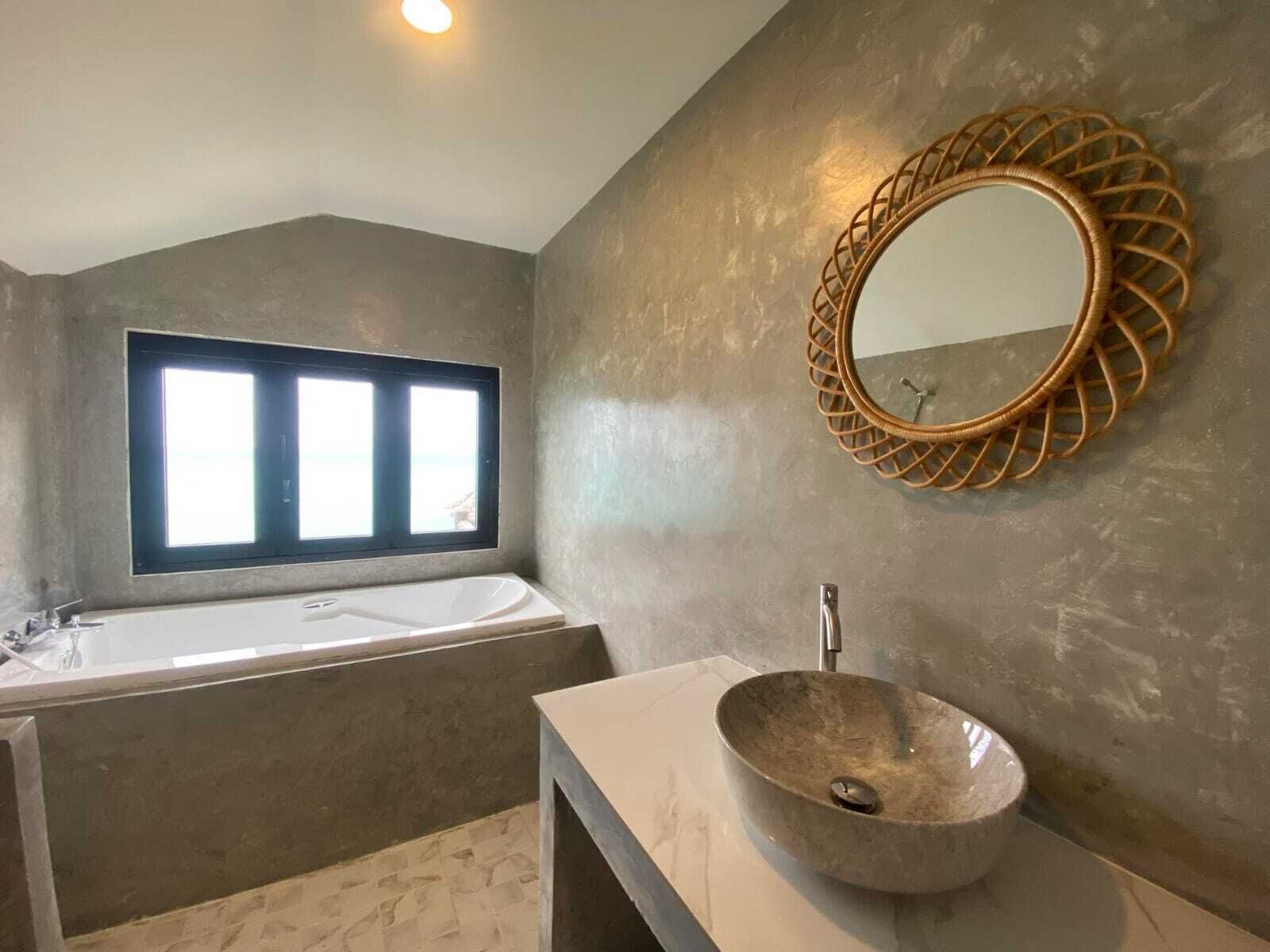A modern bathroom with a large bathtub, a round mirror with a woven frame, and a vessel sink.