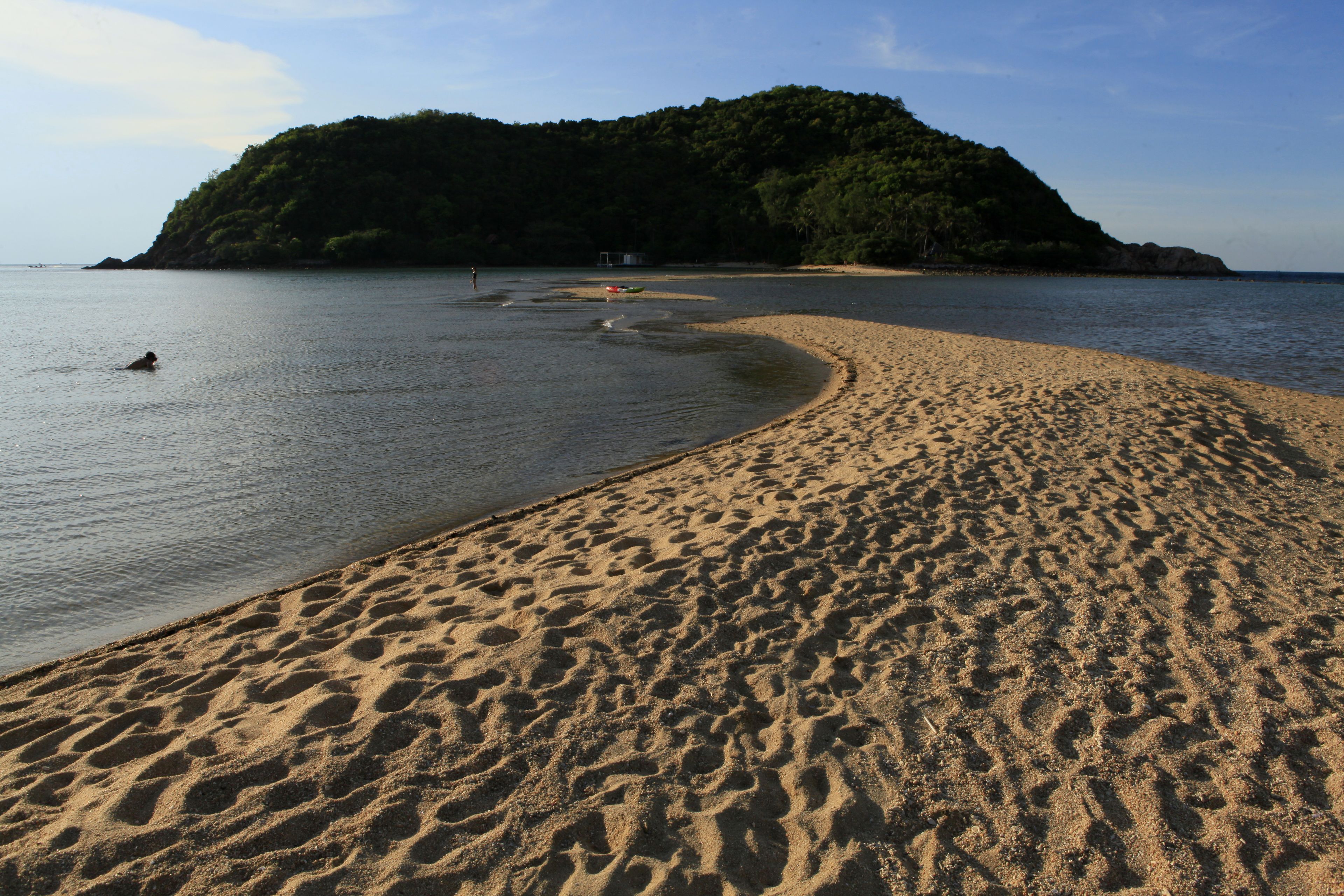 A sandy beach with gentle waves, a small island in the background, and a clear sky.