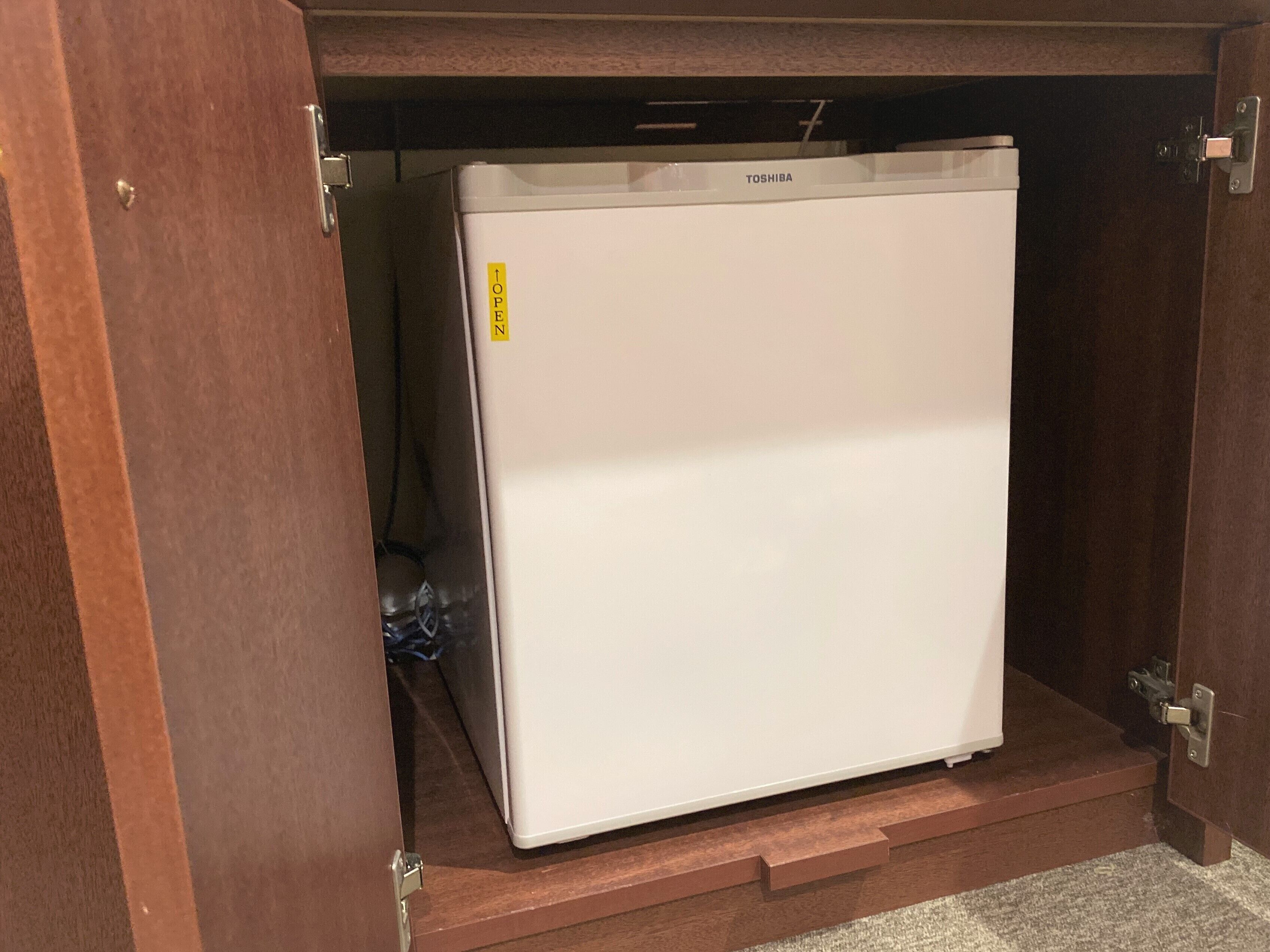 A white refrigerator under a wooden cabinet with a label that reads "TOP OPEN".