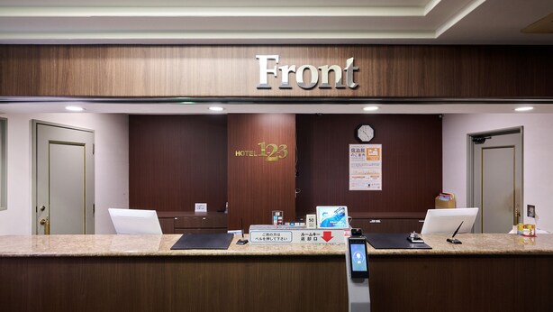 A hotel reception desk with a wooden front desk, a digital screen, and a sign indicating room number 123. - Hotel 1-2-3 Kokura (Kitakyushu)