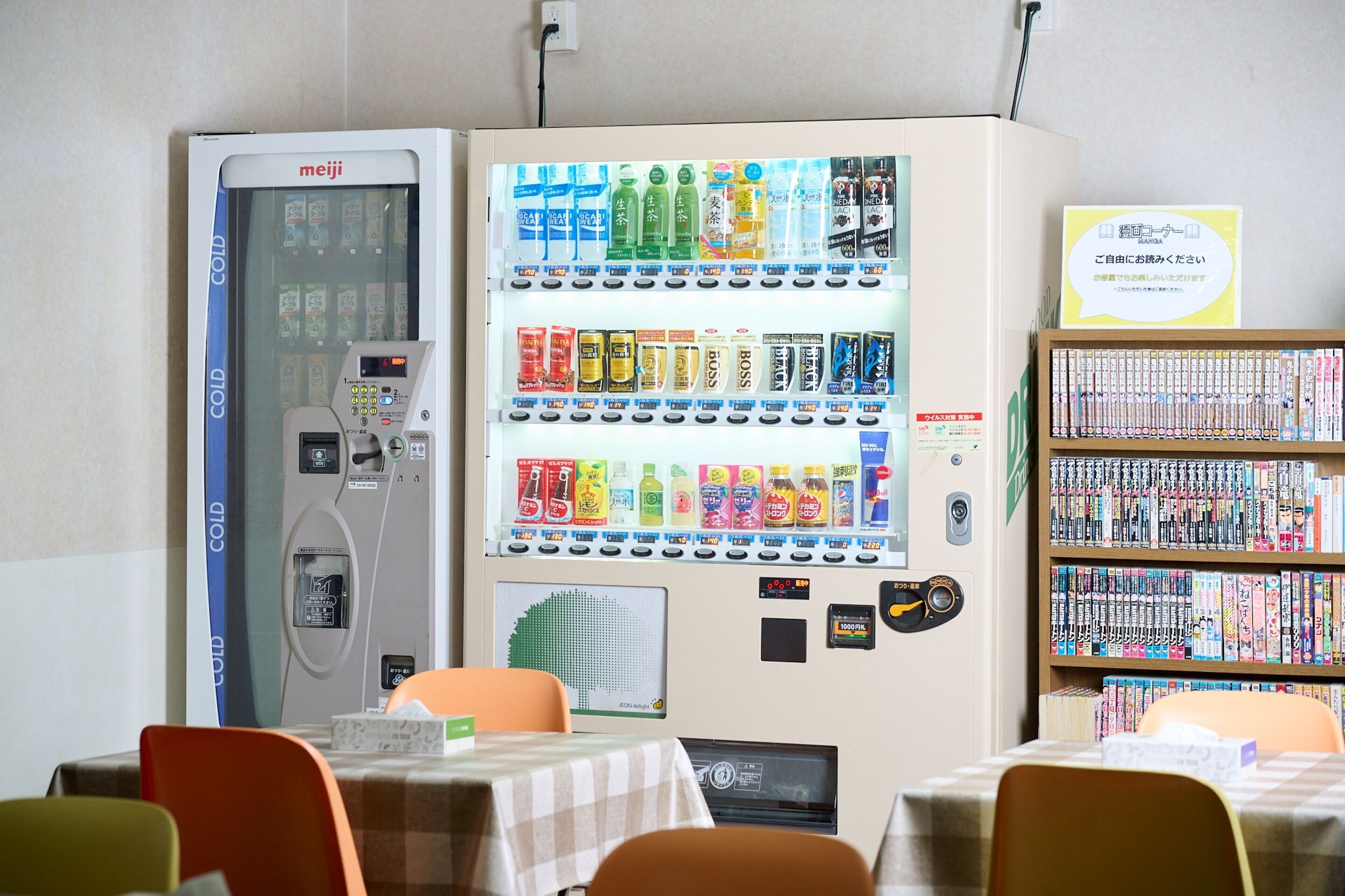 A vending machine with various drinks and snacks, a cold storage unit, and a bookshelf with books.