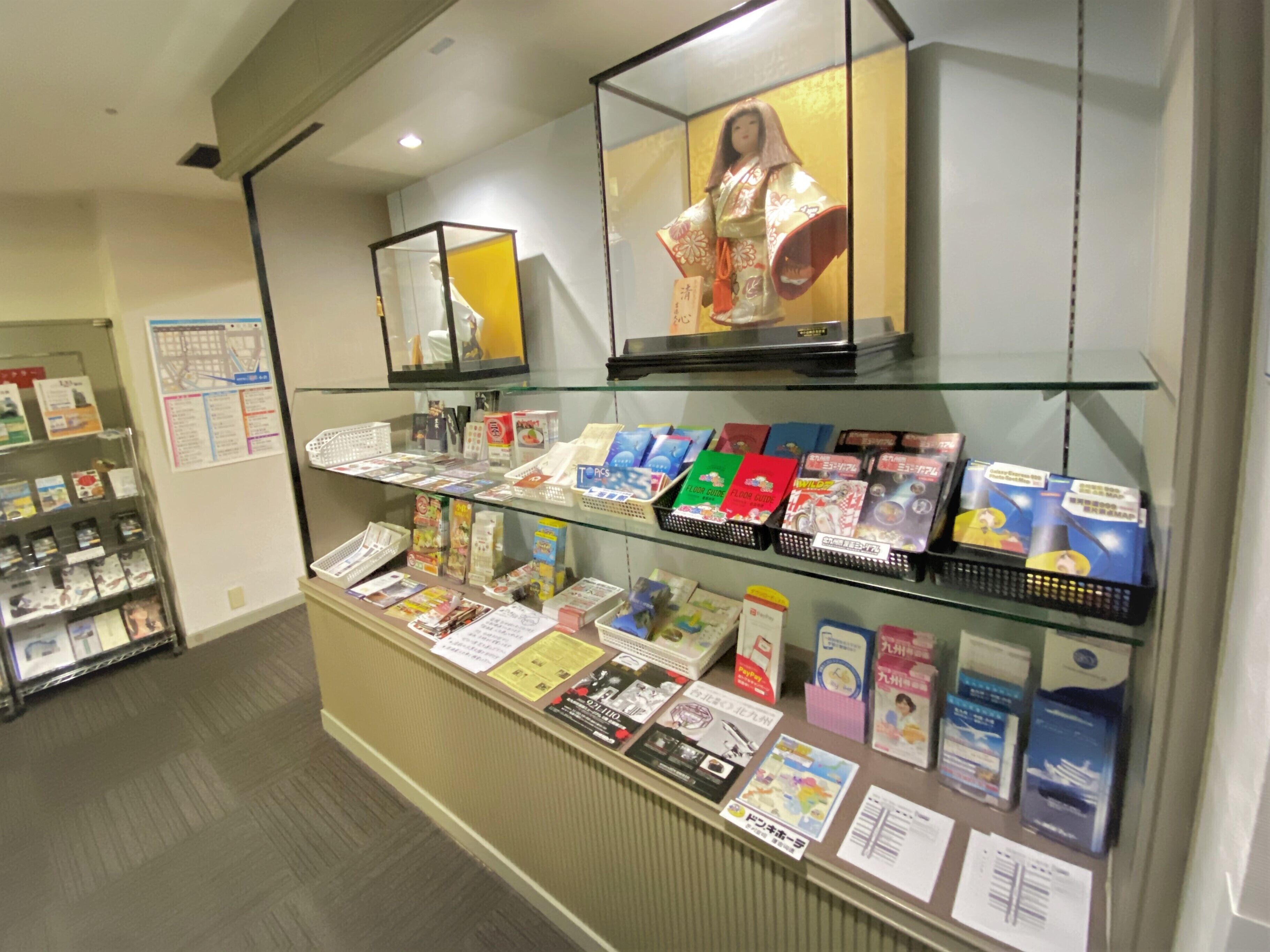 A bookstore with shelves of books and magazines, a display of postcards, and a framed artwork above the counter.