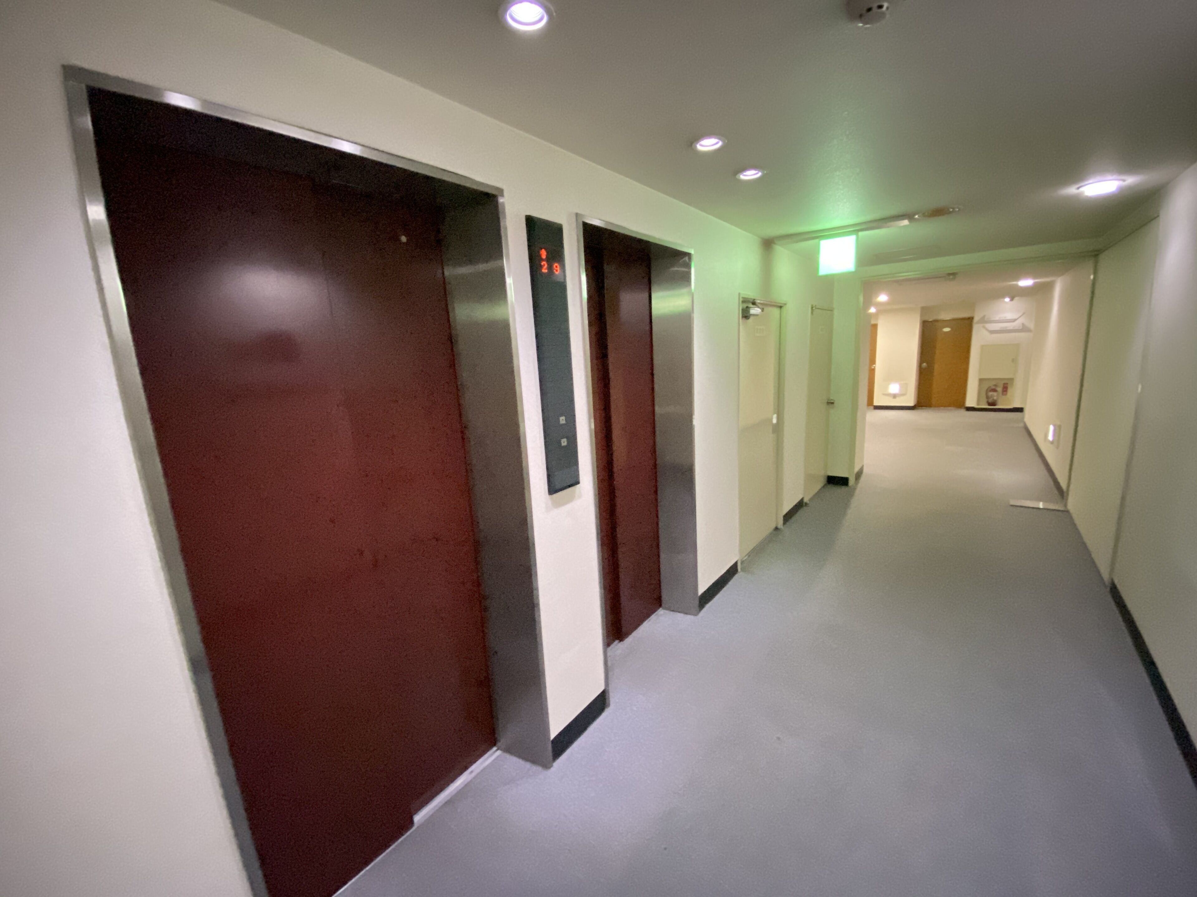 A long, narrow hallway with multiple doors, some with digital displays, and a carpeted floor.