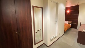 A bedroom with a wooden wardrobe, a white door, a bed with an orange blanket, and a bedside table. - Hotel 1-2-3 Kokura (Kitakyushu)