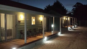 Filas de cabañas con puertas de cristal, cada una con un pequeño patio con sillas y mesas, y un área exterior cubierta con una escalera.