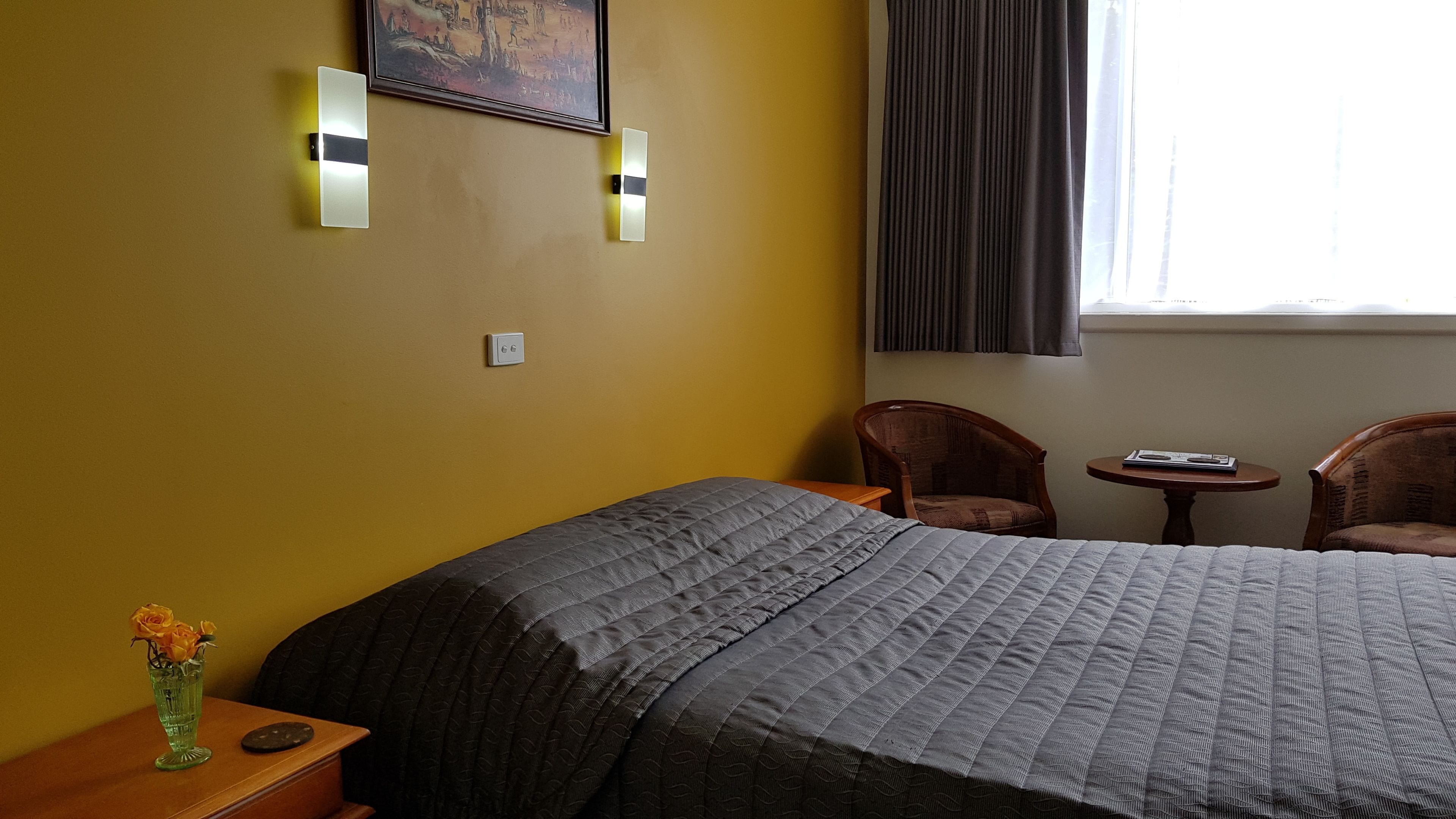 Una habitación de hotel con una cama, dos sillas, una mesita y un florero con flores.