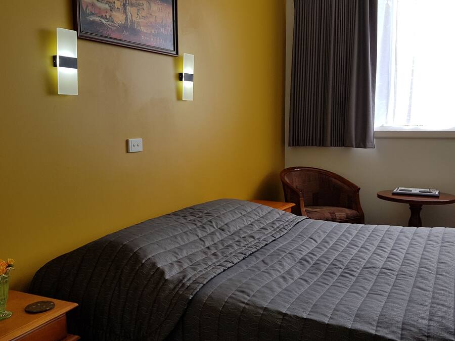 Una habitación de hotel con una cama, dos sillas, una mesita y un florero con flores.