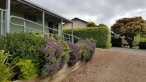 A building with a green exterior, a gravel driveway, and a variety of purple flowering plants along the side. - Daylesford Central Motor Inn (Daylesford)