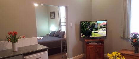 A compact living space with a kitchenette, a bed, a television mounted on the wall, and a small dining area.