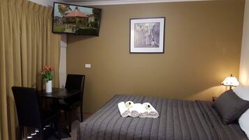 Ein Hotelzimmer mit Bett, Schreibtisch, Stuhl, Fernseher und einem gerahmten Bild an der Wand.