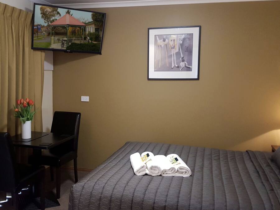 Ein Hotelzimmer mit Bett, Schreibtisch, Stuhl, Fernseher und einem gerahmten Bild an der Wand.